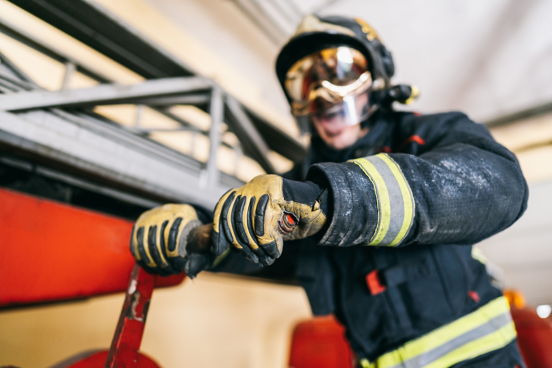 Anonymous firefighter in uniform with yellow lines and protective helmet moving red lever arm near ladder on fire truck in garage